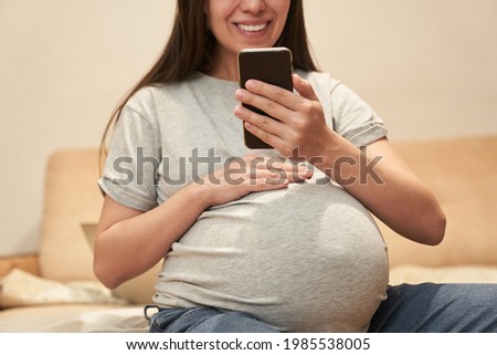 Pregnant woman at home with phone is sitting and smile, concept: video communication. High quality photo