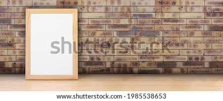 Empty frame with blank paper sheet on a wooden table and brown brick wall texture background. Banner with copy space for mock-up, product display or website header