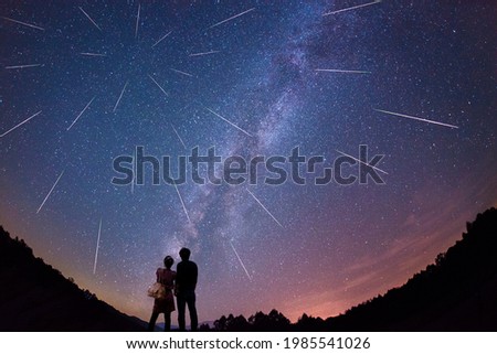 Silhouette of a young couple staring at the Milky Way and meteor shower.
