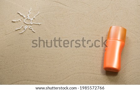 Sand texture with sun painted with cream and orange sunscreen tube. Empty space for creative design or text. Relax on the sandy beach. Holidays and travel concept