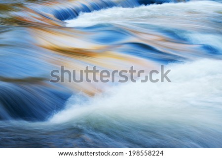 Bond Falls cascade captured with motion blur and illuminated by reflected color from sunlit autumn maples and blue sky overhead, Michigan's Upper Peninsula, USA 