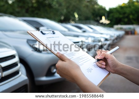 Action of a customer is signing on the agreement term of car rental service. Close-up and selective focus a human's hand with blurred background of cars in row. Business and transportation concept.