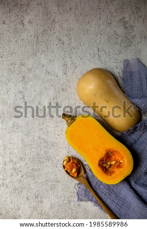 Halves of raw organic butternut squash with seeds on wooden spoon on grey napkin and abstract background