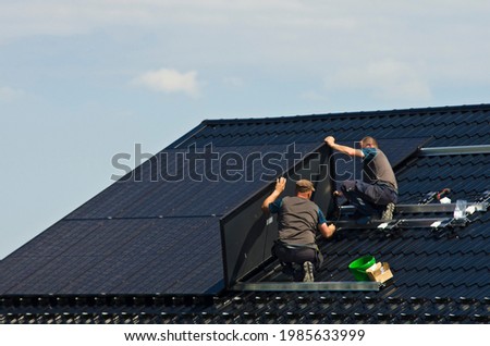 Installing new black solar panels on the metal roof of a private house. Ecology, renewable energy and green sustainable source of power abstract. Royalty-Free Stock Photo #1985633999