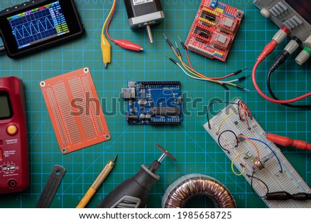 Top view of electronic lab bench showing an Arduino UNO microcontroller surrounded by basic electronics tinkering tools Royalty-Free Stock Photo #1985658725