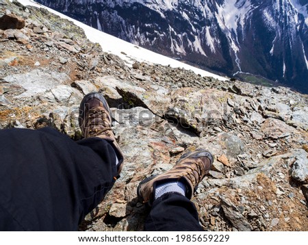 Man feet on rock rocks in mountain trekking boots over a cliff in the snowy mountains. Epic first person landscape photography. The concept of loneliness and solitude.