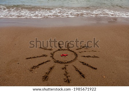 symbol of the sun and a plane by the sea. Painted sun on the sand, sea coast, figure of a red plane, sea waves.