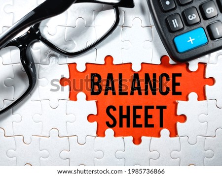 Business concept.Text BALANCE SHEET with glasses and calculator on jigsaw puzzle and red background