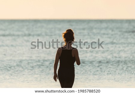 Silhouette of a young woman on the beach, at sunrise. Rear view of the girl enjoying the beautiful sunset on the beach. Travel destination. Concept summer vacation