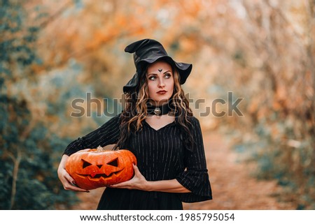 Girl dressed as witch holding pumpkin in her hands on forest background.