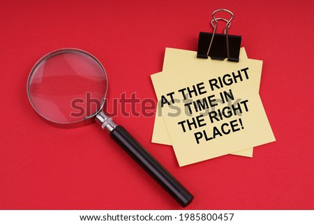 Business and Economics. On a red background, a magnifying glass and a sticker with the inscription - At the right time in the right place