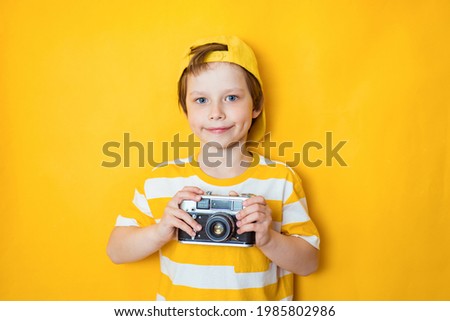 Say cheese. Young active kid boy takes photo with retro camera, poses against yellow background, has awesome trip, explore new places