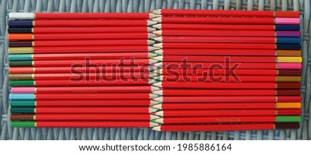Large number of red bodied rainbow multi coloured wooden pencils. Arranged pointed end to end in a striped parallel line collection. Flat lay from above. Textured abstract background or pattern