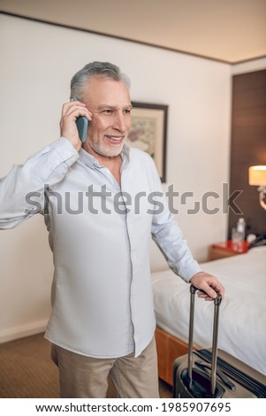Smiling mid-aged gray-haired businessman talking on the phone and looking contented