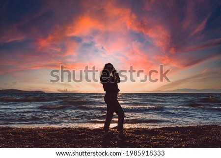 Woman silhouette at sunset, woman posing on the beach and blushing clouds in the background with sunset.
