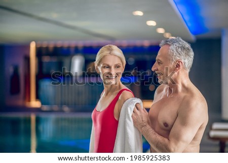 Gray-haired man drying his wife with a towel after swimming in a pool