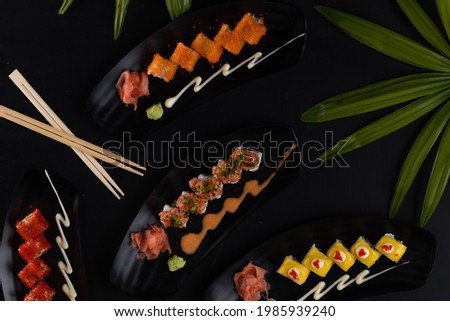 Top view mix of sushi, Japanese food over black table with tropical leaves