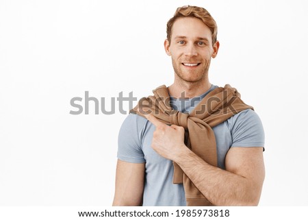 Look that way. Smiling redhead man with muscles big biceps, pointing at upper left corner, showing advertisement on product on copy space, standing over white background