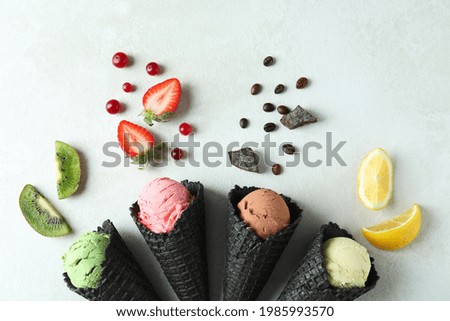 Black cones with ice cream and ingredients on white textured background