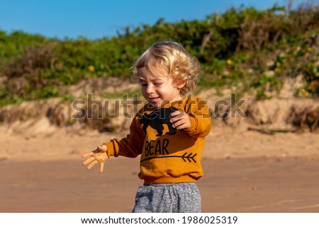 BLONDE CHILD PLAYING ON THE BEACH.
