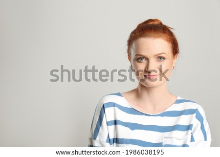 Candid portrait of happy red haired woman with charming smile on light background, space for text