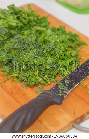The photo shows a picture of healthy raw food. There are young and fresh greens here. This is a bunch of parsley and a bunch of dill. The greens are lying on a wooden board along with a knife