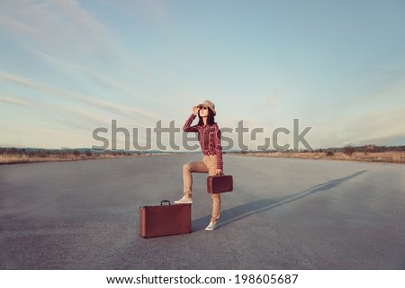 Young traveler hipster woman with retro suitcase looks through binoculars on road