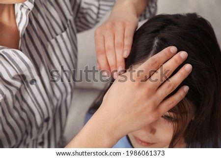 Mother examining her daughter's hair indoors. Anti lice treatment