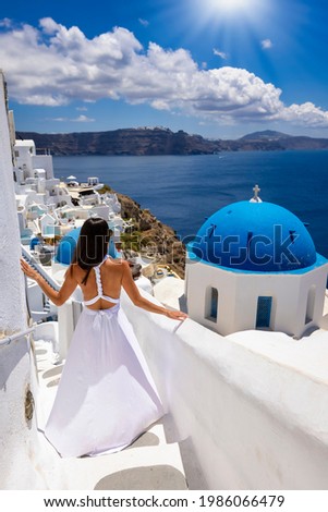 A woman in a white dress walks through the whitewashed houses of  Oia at Santorini island, Cyclades, Greece, during her summer holidays Royalty-Free Stock Photo #1986066479