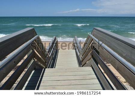 A wooden staircase with handrails leads to the ocean. Royalty-Free Stock Photo #1986117254