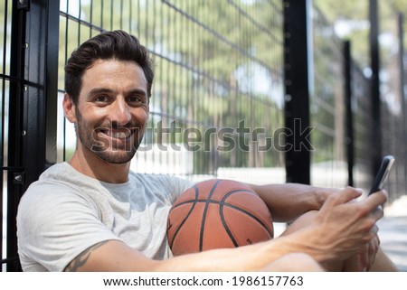 smiling basketball player using mobile phone while taking a break