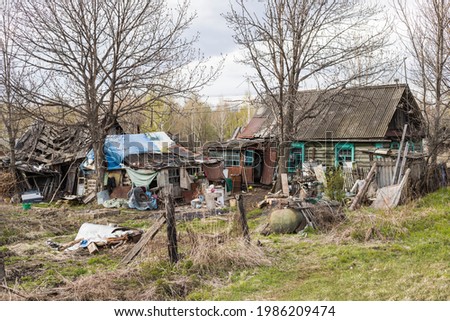A dilapidated old residential wooden house surrounded by garbage around the house. Poverty in Russia. Royalty-Free Stock Photo #1986209474