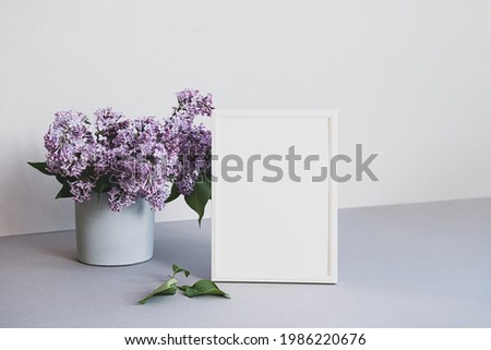 Mock up photo frame in minimalistic interior. Modern still life scene of white frame and bouquet of lilacs. Concept trendy home decor. Banner in pastel colors.