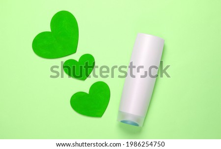 Shampoo bottle with hearts on green pastel background. Beauty care. Top view. Minimalism
