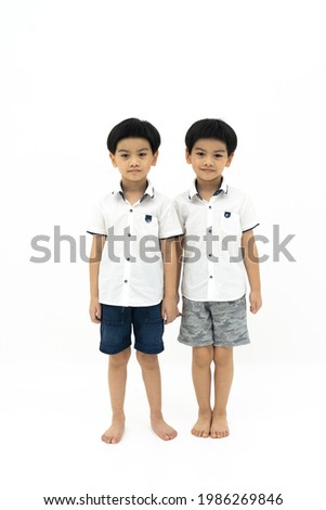 Picture of twin asian boys standing together on white background. Looking at camera.