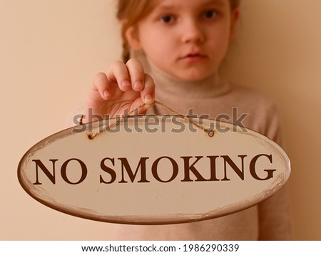 Child holds a sign with the inscription No smoking. Children Protection Day. The child has an aversion to the smell of smoking, tobacco, smoke. Protecting the child from bad habits. Focus on the plate