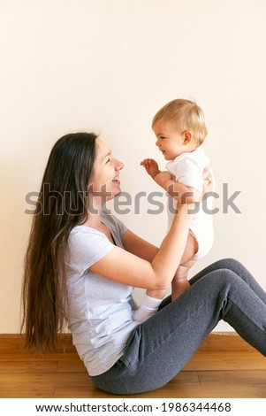 Laughing mom sits on the floor in the room and picks up a little girl
