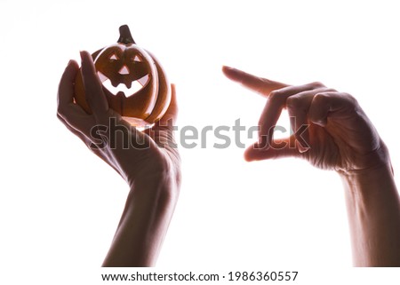It's Halloween, concept. Halloween little pumpkin with face in women's hands, pointing finger at the pumpkin, isolated on white, contour lighting, contrast.