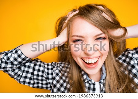 Cheerful girl in a shirt clutches her head with her hands laughing and looking at the camera