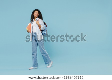 Full length young happy african american girl teen student wear denim clothes backpack hold book walk go isolated on blue background studio portrait Education in high school university college concept