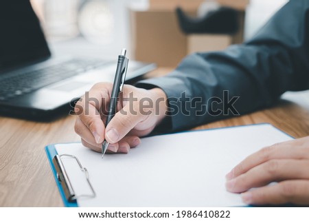 A man checking the delivery list and writing on the white paper clip board file and looking data form computer laptop to deliver items to customers Royalty-Free Stock Photo #1986410822