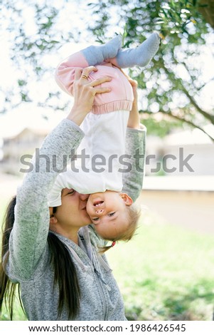 Smiling mom lifts her little girl upside down and kisses her on the cheek
