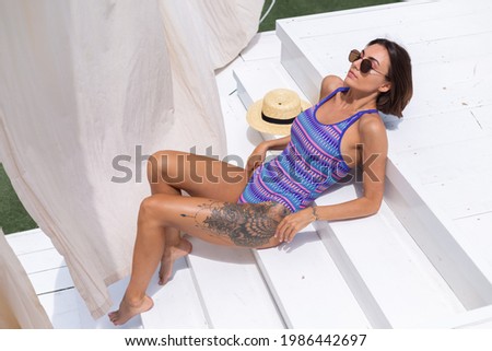 Beautiful woman in swimsuit at backyard pool at summer sunny day enjoying amazing warm weather, catching sun rays