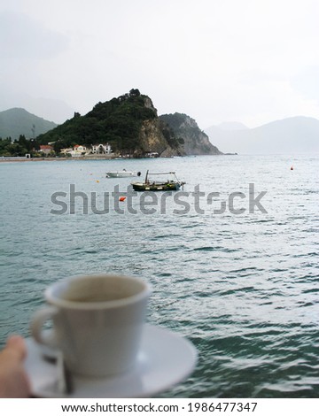 Beautiful mediterranean landscape - town Petrovac, Montenegro. Rainy day with cup of coffee. Boat and mountains view.