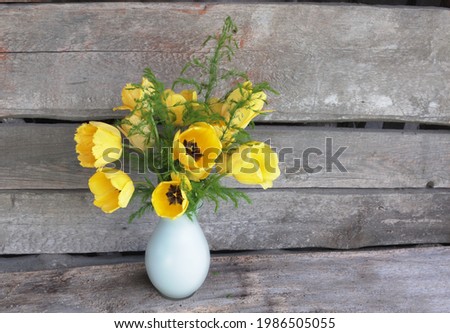 A large bouquet of bright yellow tulips with green leaves in a white vase. The background is rough old boards. Place for an inscription.