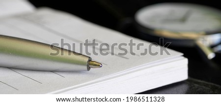 A notebook or diary, a ballpoint pen and a wrist watch are on a black table. Concept of memoir, bequest or daily routine planning. Web banner. Selective focusing. Macro Royalty-Free Stock Photo #1986511328