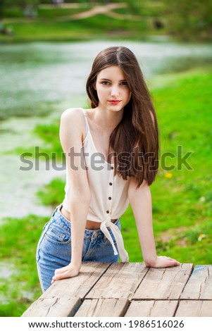 Portrait of a young beautiful girl in posing against the background of a pond in a summer park