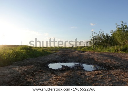 Rut dirt road across steppe after rain against sunset sky background. Russia Royalty-Free Stock Photo #1986522968