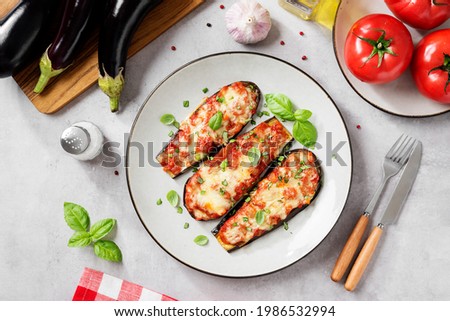 Baked eggplant with mozzarella cheese, chopped tomatoes and fresh basil leaves. Vegetarian food recipe. Light gray background, top view.  Royalty-Free Stock Photo #1986532994