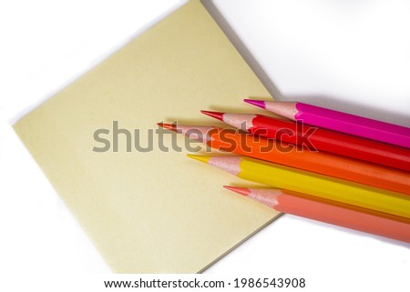 Colored pencils on a white background with a yellow sticker, close-up, place for text.